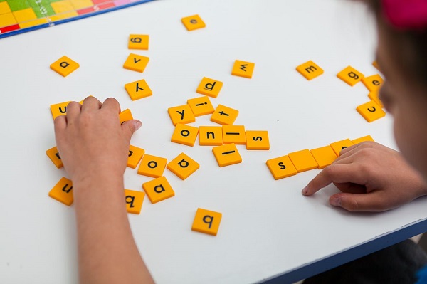 A Small Boy Trying To Frame Words By Using Alphabet Blocks.