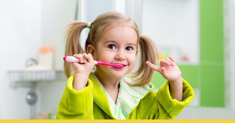 A cute little girl brushing her teeth infront of the mirror in the bathroom.