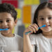 Two Cute Happy Kids Brushing Their Teeth Infront Of Mirror Representing The Healthy Teeth Concept.