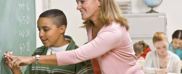 A teacher helps the student to write on the blackboard in the classroom.