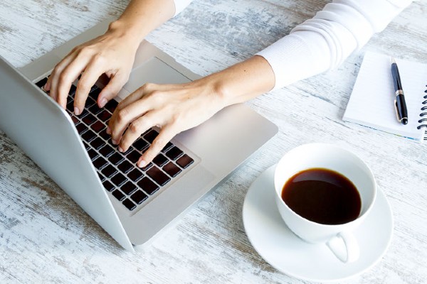 Cropped shot of female hands typing on her laptop while writing.