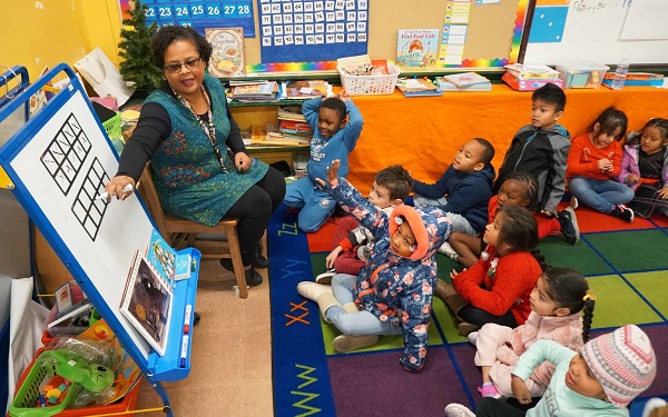 A kindergarten teacher is teaching kids with a white board, abacus and markers in the classroom.