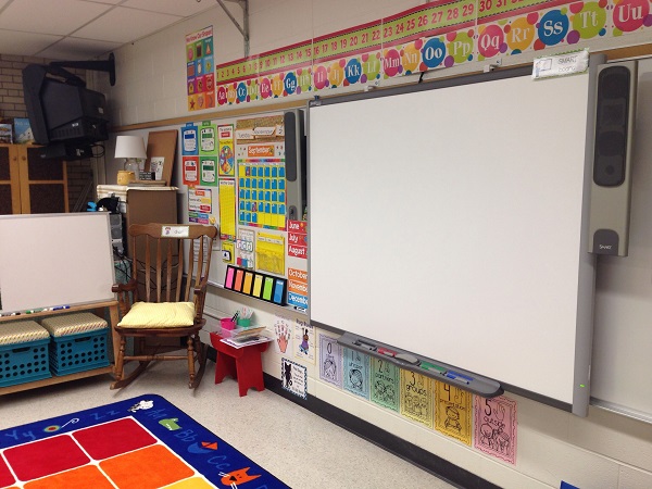 A kindergarten classroom filled with smartboard, colorful learning charts, wooden chair and other kid friendly items.