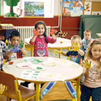 Kids surrounded the round table with some colorful paints coated on their hands, seems they are in the mid of the painting class.