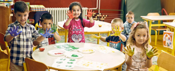 Kids surrounded the round table with some colorful paints coated on their hands, seems they are in the mid of the painting class.