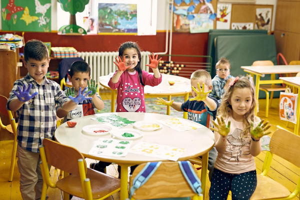 Kids surrounded the round table with some colorful paints coated on their hands, seems they are in the mid of the painting class.