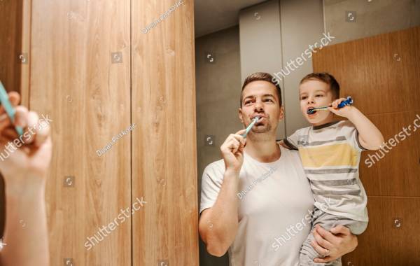 In a bathroom, a loving father is brushing his teeth with his son in his arms.